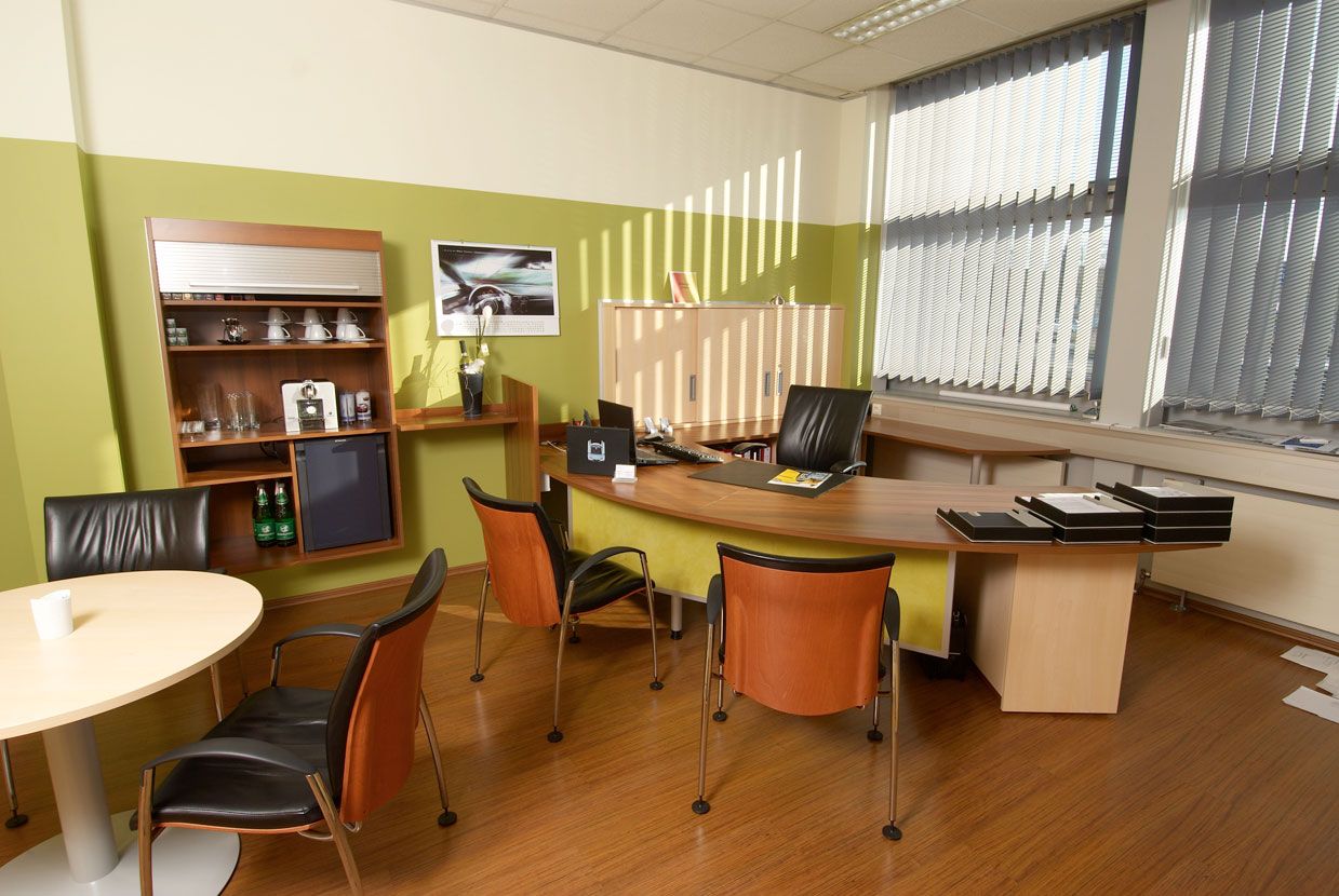 Büro mit grüner Wandfarbe und schwarz-braunen Lederstühlen