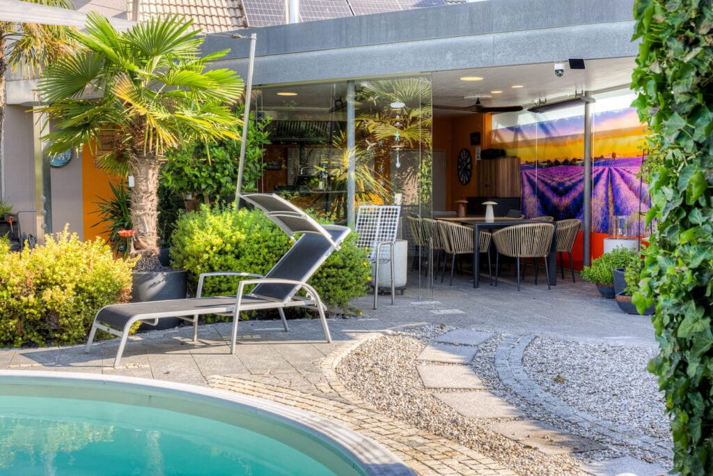 Outdoor-Bereich mit Pool, loungemöbeln, bepflanzten Kübeln und Essbereich, umgeben von Steinen und Rasenflächen.
