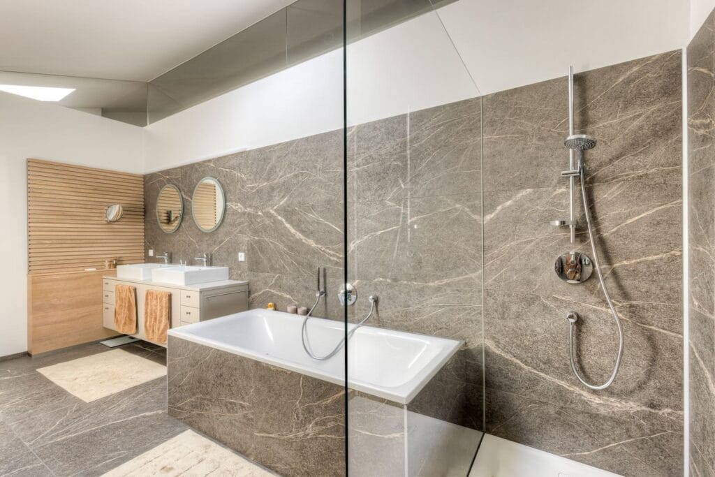 Modernes Badezimmer mit Dusche und Badewanne, dunklen Steinfliesen, heller Holz1er mit Ablage und natürlichem Licht durch Dachfenster.