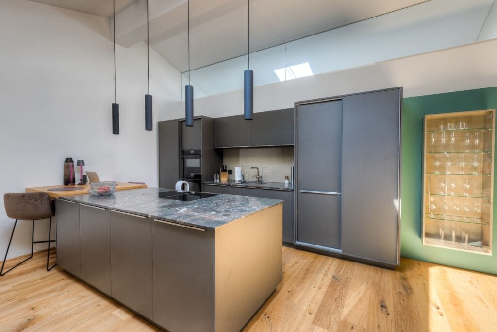 Moderne Küche in Dachgeschosswohnung mit Holz- und Metalloberflächen, hellen Wänden und eleganten Pendelleuchten.