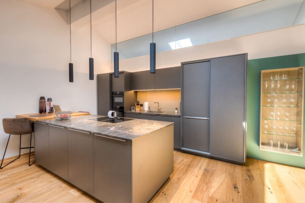 Moderne Küche in Dachgeschosswohnung mit Holz- und Metalloberflächen, hellen Wänden und eleganten Pendelleuchten.