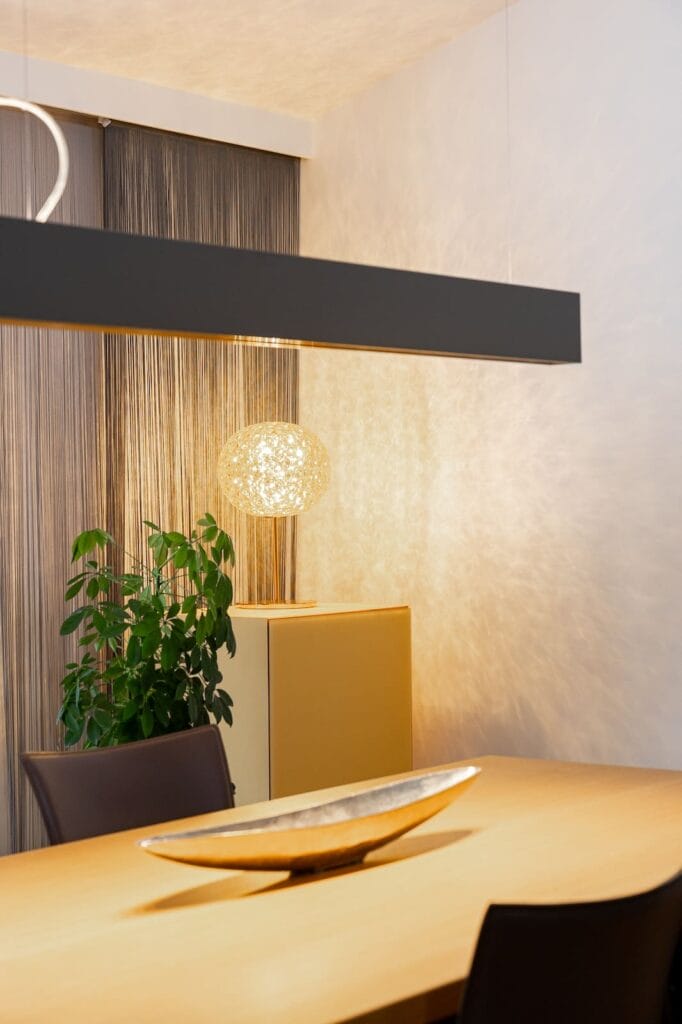 Esszimmer mit einem Holztisch, Stühlen in Dunkelbraun, einer Pendelleuchte und pflanzlicher Dekoration.