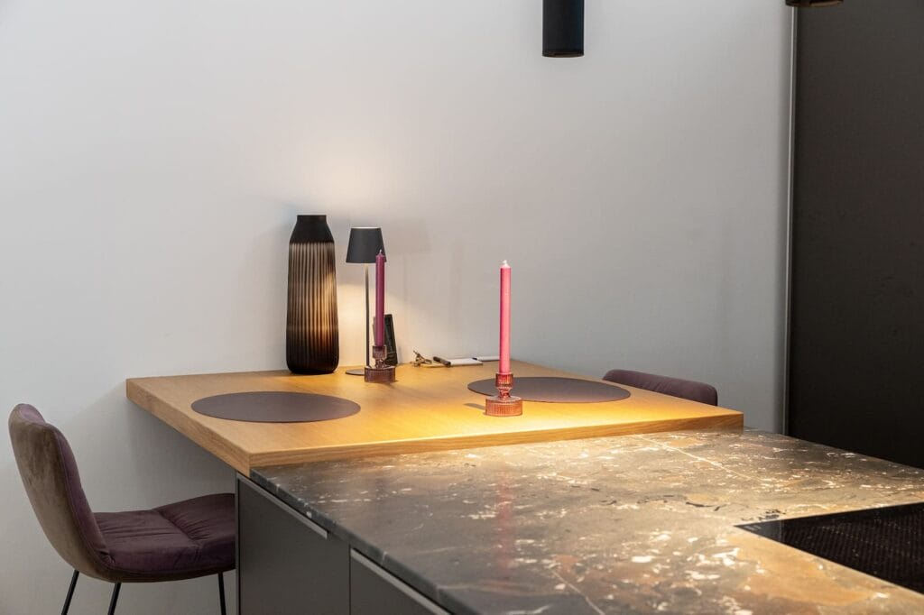 Moderne Küche mit Holz- und Steinoberflächen, eleganter Tischbeleuchtung und einer Kombination aus Stuhl und Tisch in sanften Farbtönen.
