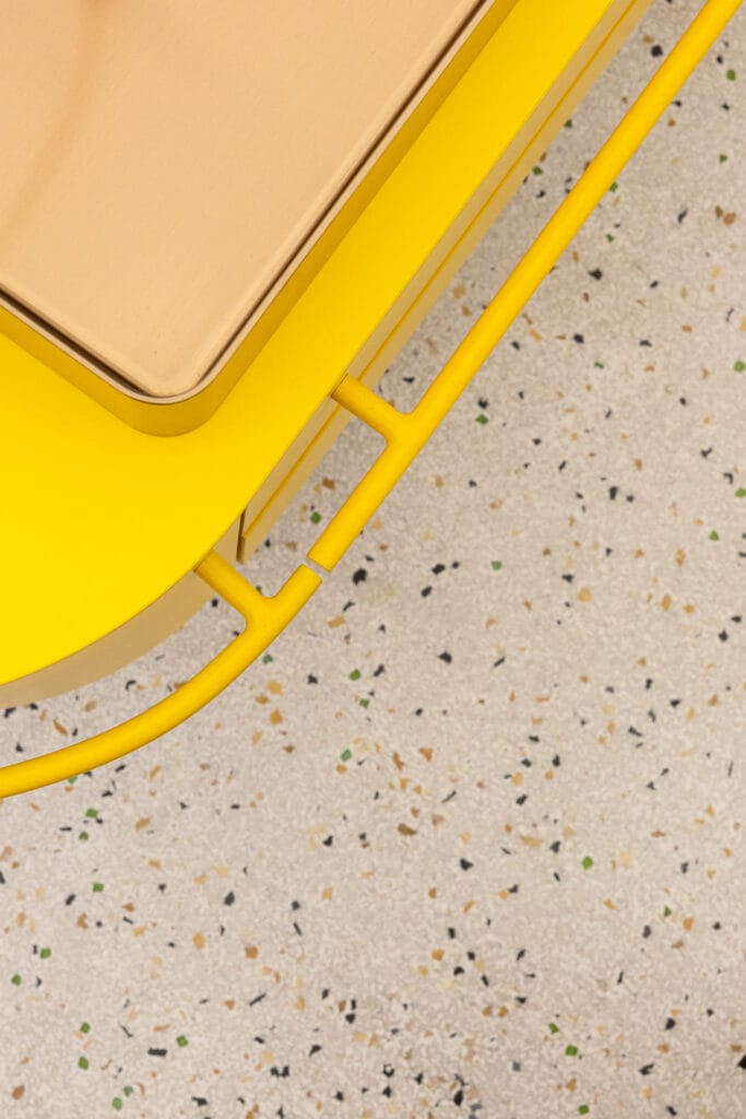 Ein gelbes Möbelstück mit einem bronzenen Waschbecken und einem bunten, sprenkelnden Terrazzo-Boden