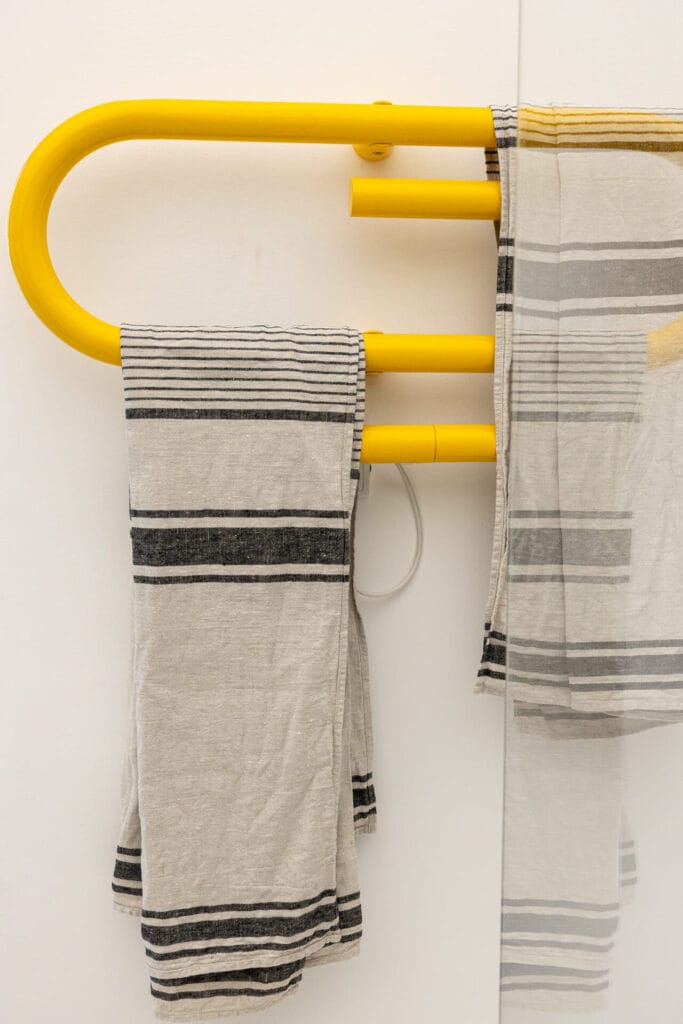 Ein Handtuchhalter aus gelbem Material mit gestreiften Handtüchern vor einer weißen Wand.