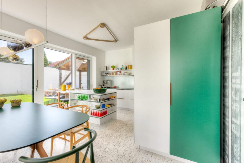 Küche mit modernem, weißen Design, grünen Schranktüren, Boden aus Terrazzo und großen Fenstern, die in den Garten blicken.