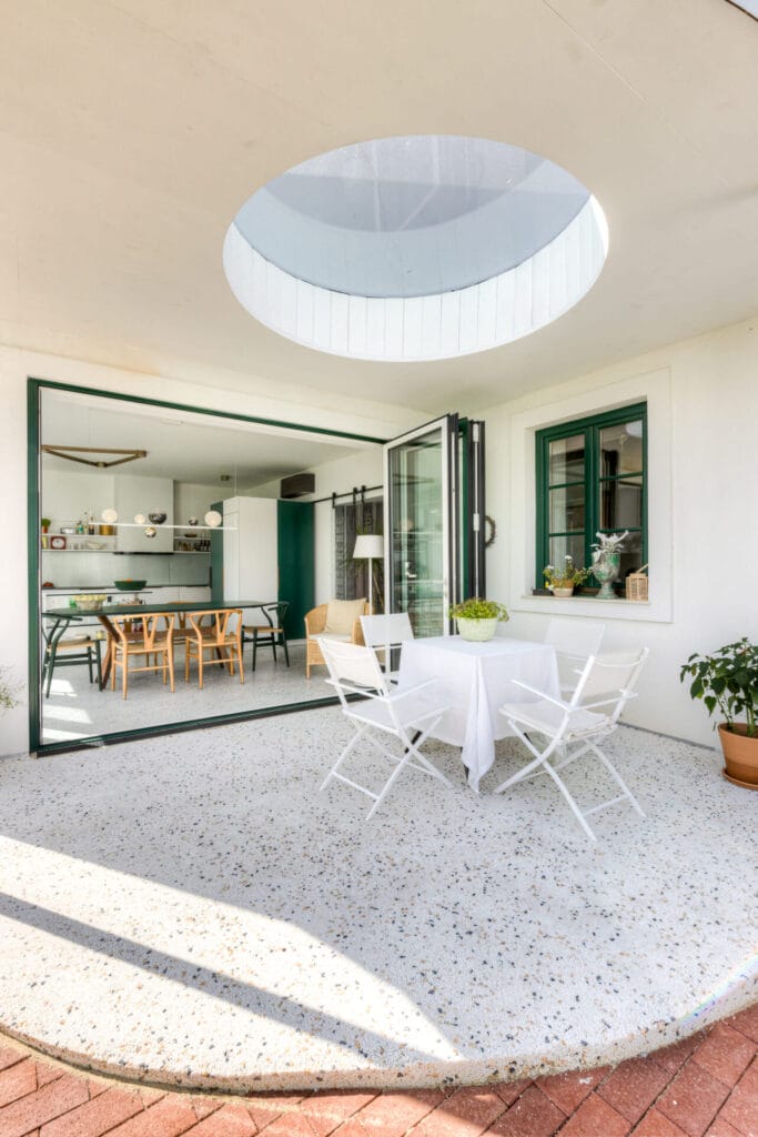 Terrasse mit runder Glasoberlicht, weißen Möbeln und Sicht auf den angrenzenden Wohnraum mit schwarzen Elementen.