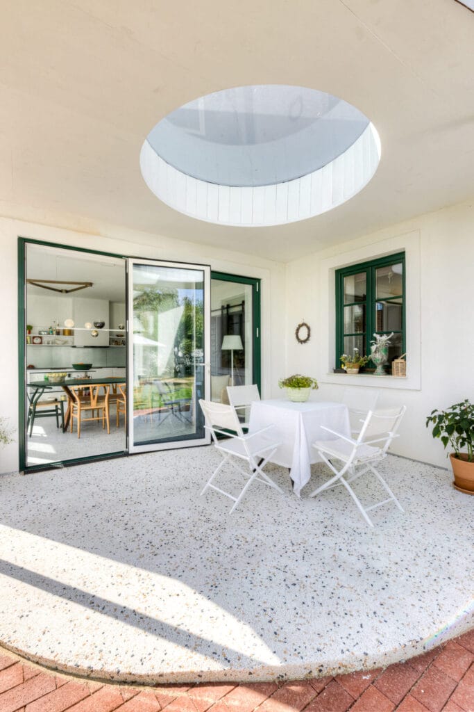 Terrasse mit runder Glasoberlicht, weißen Möbeln und Sicht auf den angrenzenden Wohnraum mit schwarzen Elementen.