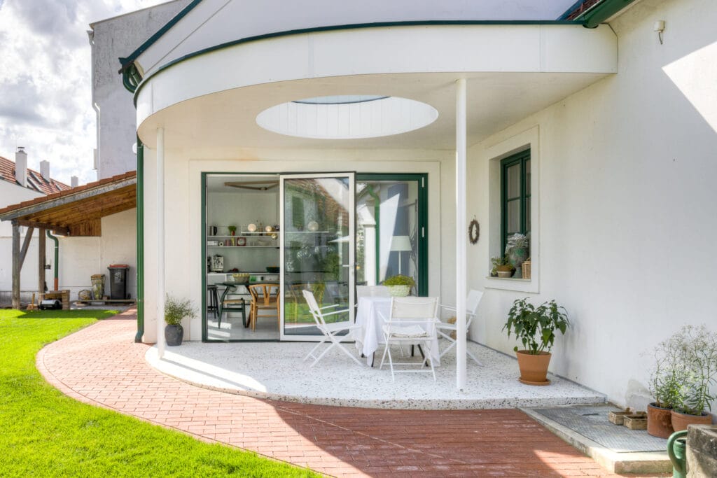 Terrasse mit runder Glasoberlicht, weißen Möbeln und Sicht auf den angrenzenden Wohnraum mit schwarzen Elementen.