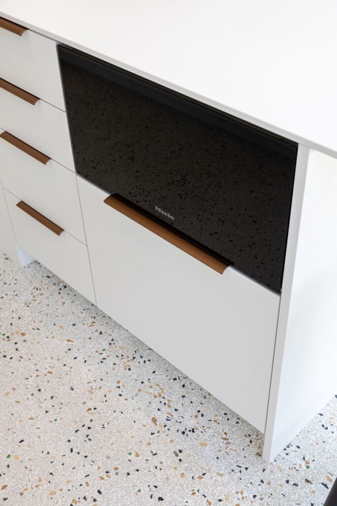 Moderne Küche mit weißen Schränken, bronzenen Griffen und einem integrierten Getränkekühlschrank für Flaschen und Tellerwärmer.