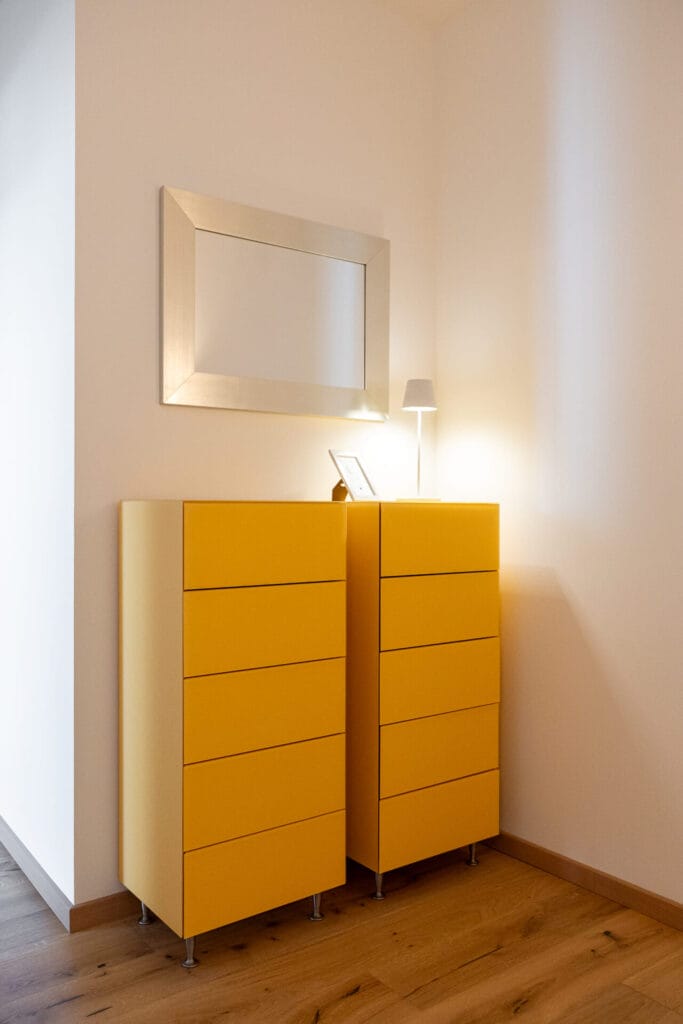 Gelbes Möbelstück mit Tischlampe und einem Spiegel an der weißen Wand.