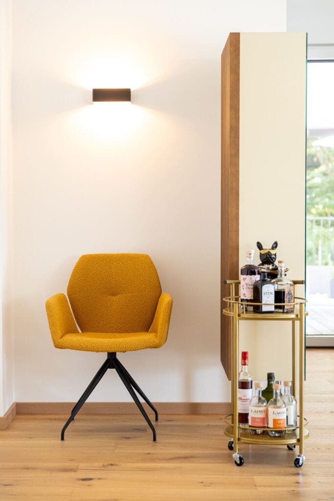 Sitzbereich mit einem gelben Stuhl und einem goldenen Servierwagen, Holzfußboden und helle Wandgestaltung.