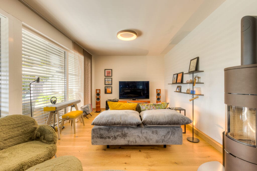 Ein Wohnraum mit einem grauen Sofa, Holzboden, einem Kamin, TV-Bereich und dekorativen Wandregalen.