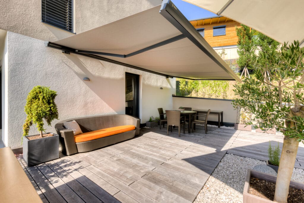 Zweite Terrasse mit Überdachung, einer grauen Sitzgarnitur mit orangen Auflagen und Pflanzen.