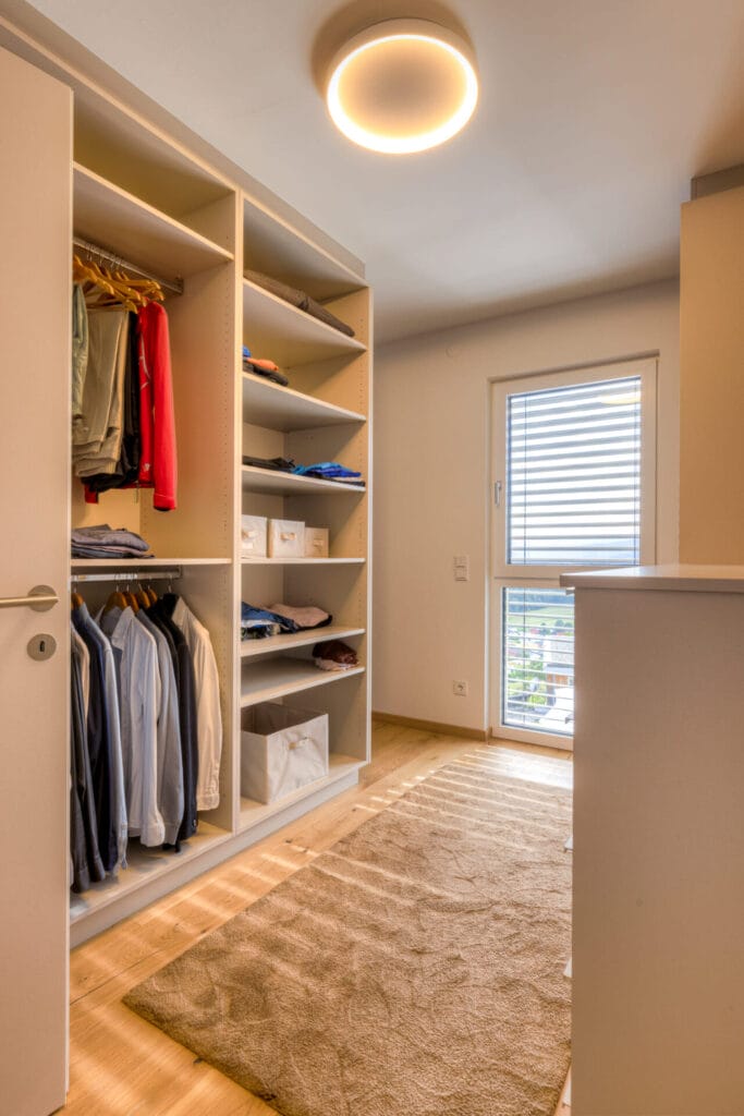 Begehbarer Kleiderschrank ohne Fronten, Holzfußboden und Teppich.