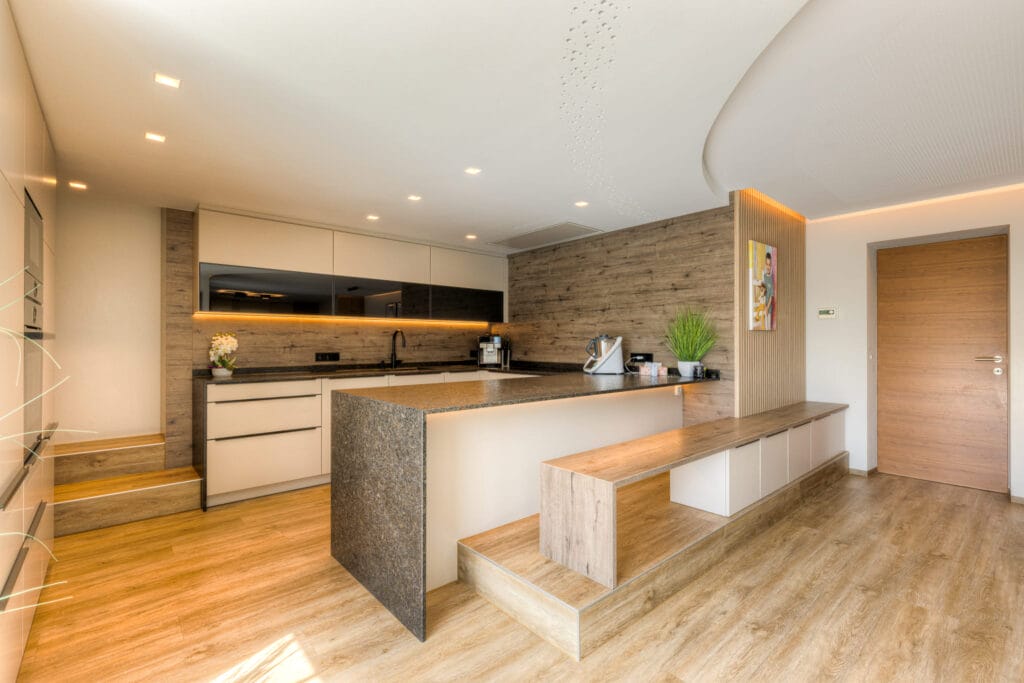 Moderne Küche mit Kücheninsel aus Stein, weißen Schränken, Holzpaneelen und warmem Licht, kombiniert mit einem Holzfußboden.