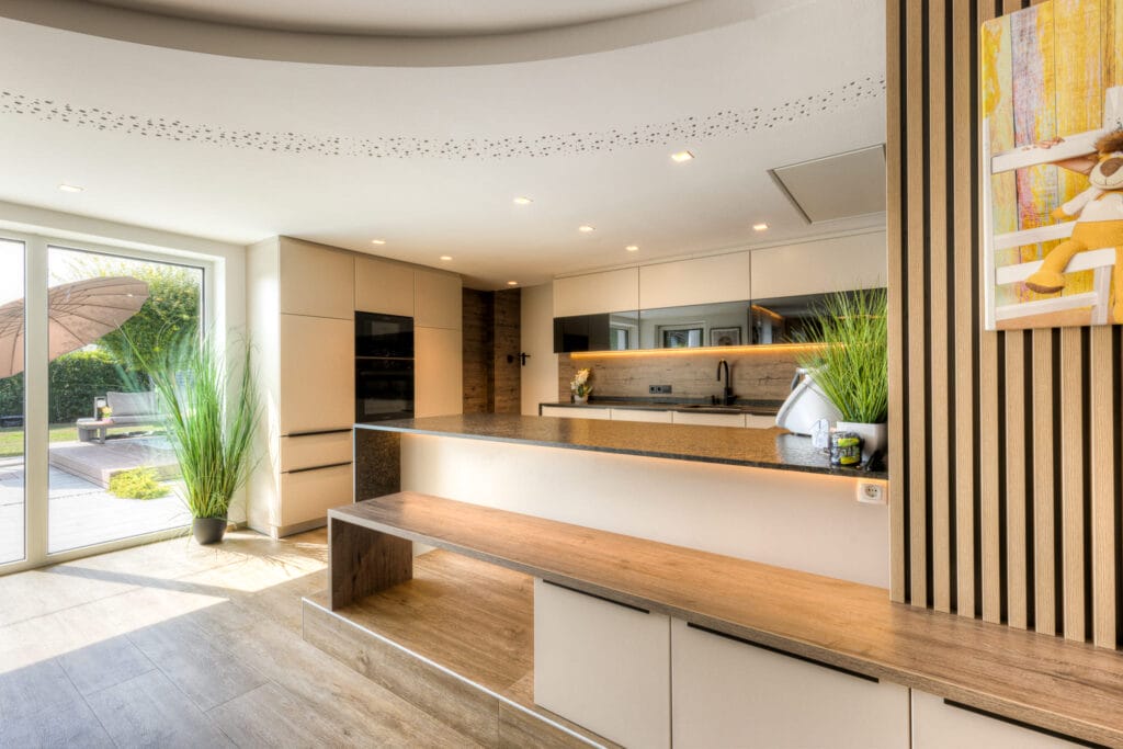 Moderne Küche mit Kücheninsel aus Stein, weißen Schränken, Holzpaneelen und warmem Licht, kombiniert mit einem Holzfußboden.