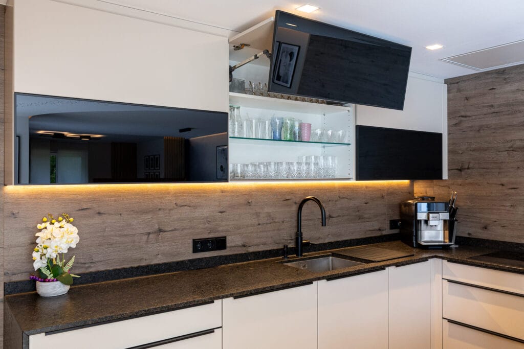 Moderne Küche mit hellem Holzdekor, eleganter schwarzer Arbeitsplatte, gläsernen Oberschränken und einer integrierten Kaffeemaschine.