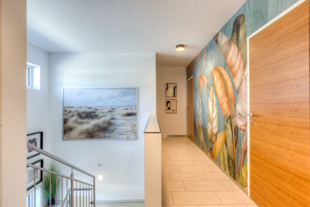 Heller Wohnraum mit Treppe, grauem Fliesenboden und farbenfrohem Wanddesign, ergänzt durch große Fenster und Kunstwerke.