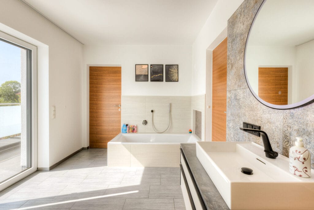 Helles Badezimmer mit moderner Wandtapete und rundem Spiegel, Aufsatz-Waschbecken und Badewanne