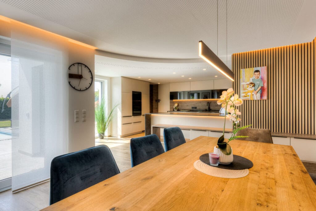 Offene Küche mit Essbereich, hellen Holz- und Neutralfarben, minimalistischen Möbeln und Holzvertäfelung an der Wand.