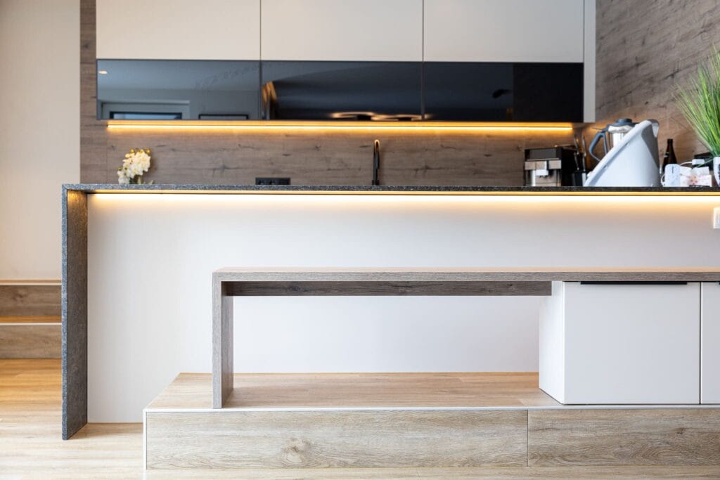Moderne Küche mit Holz- und Granitoberflächen, Einbauküchenschränken in hellen Tönen und LED-Beleuchtung.